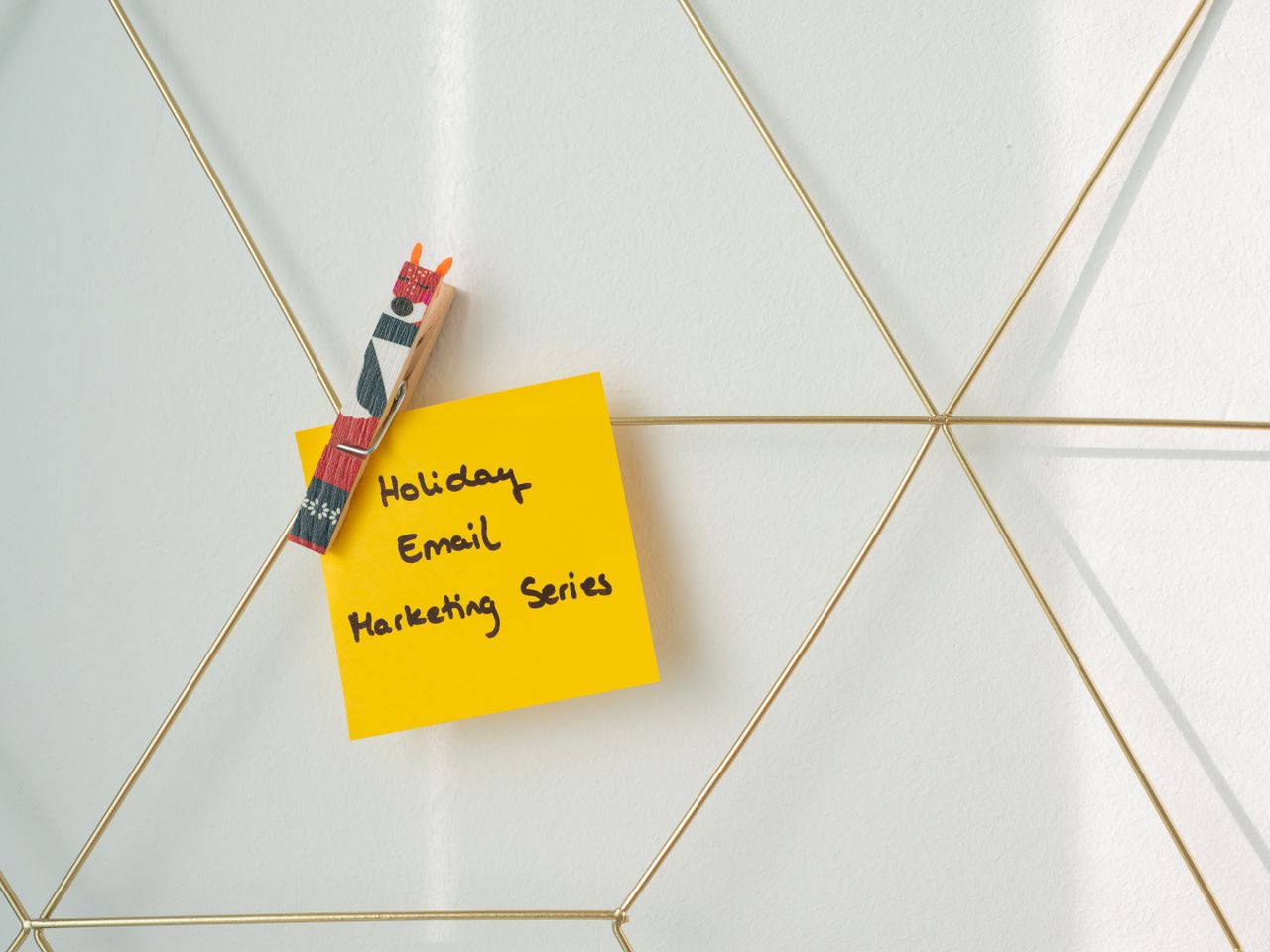 Post-it jaune vif avec un message de marketing par email pour les fêtes, fixé sur un mur en fil de fer.